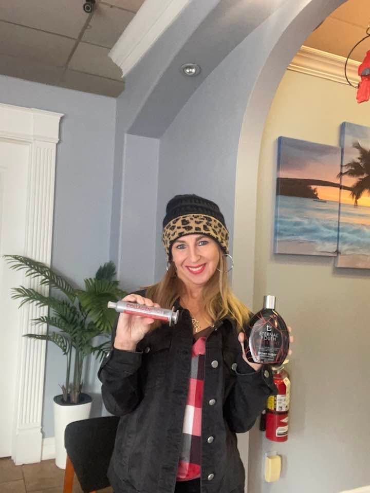 Woman indoors holding a small award and a bottle, smiling beside a wall painting and fire extinguisher.