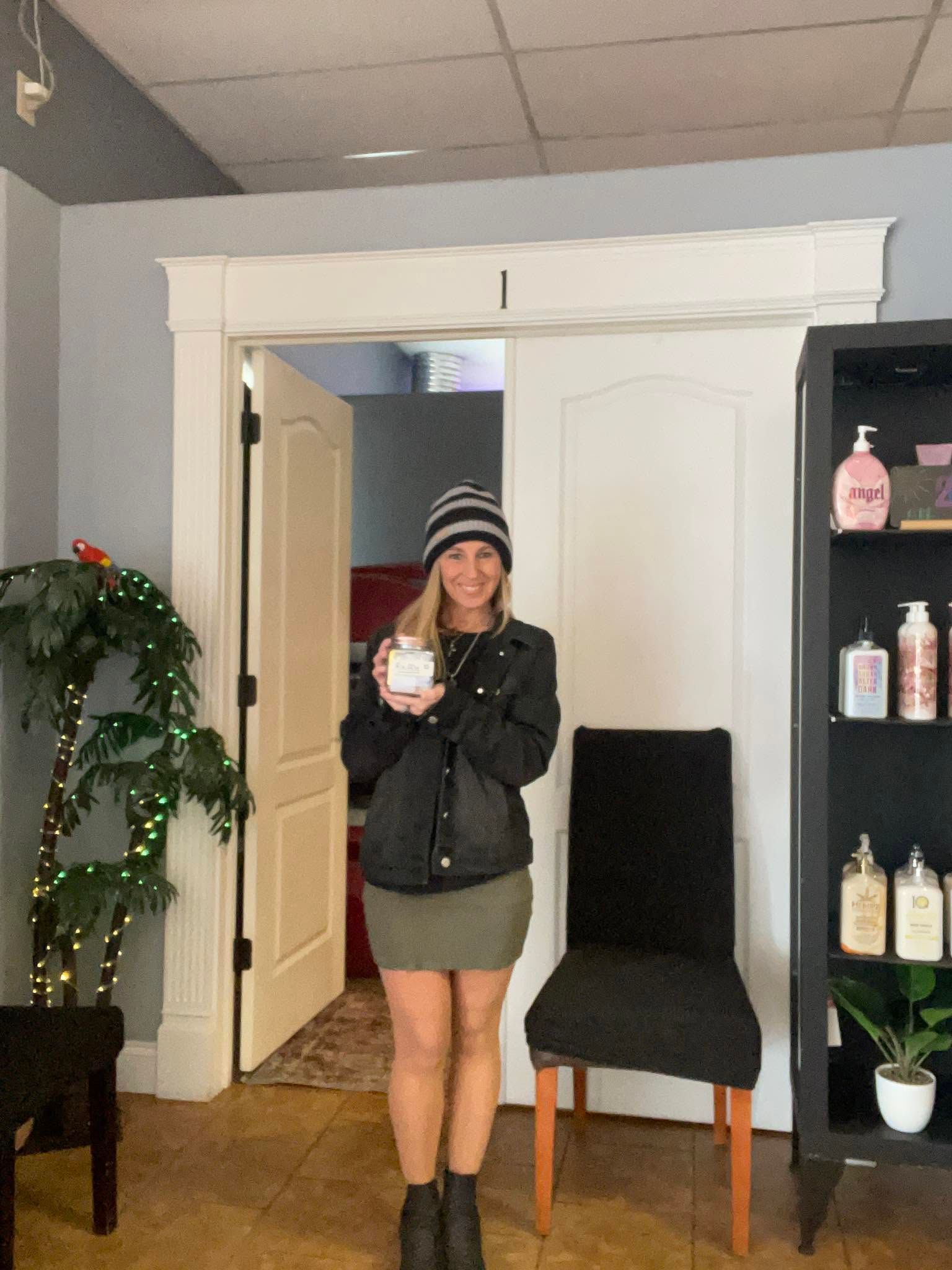 Person standing in a room, holding a small white item, with a plant, chair, and shelf in the background