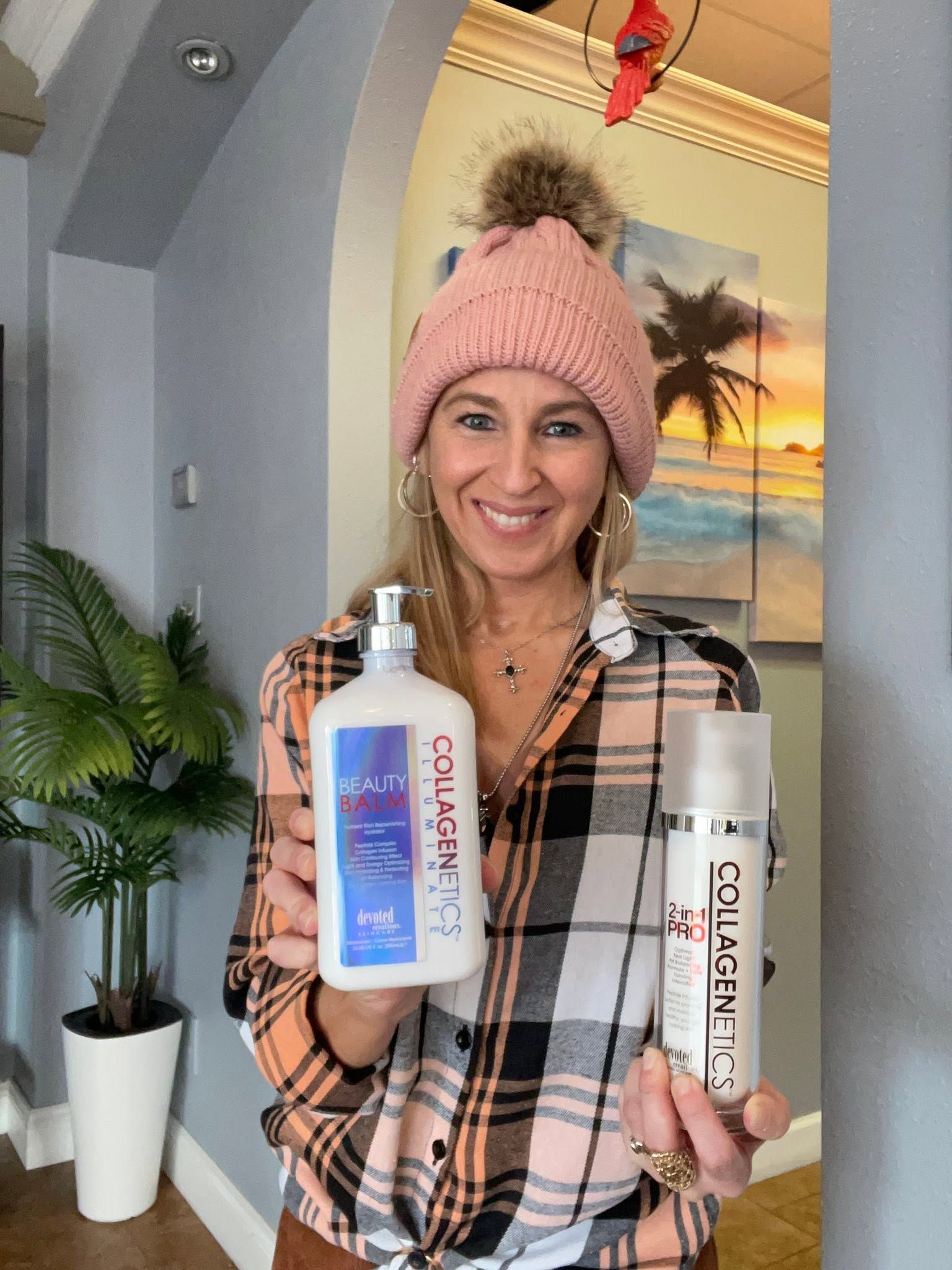 Woman smiling indoors, holding two cleaning product bottles in front of a sunset beach mural.