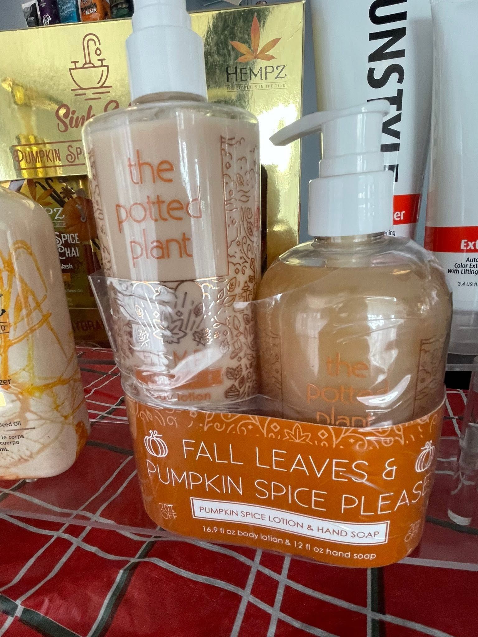 Two Bath & Body Works pumpkin spice hand soaps on a plaid tablecloth with autumn decor behind.