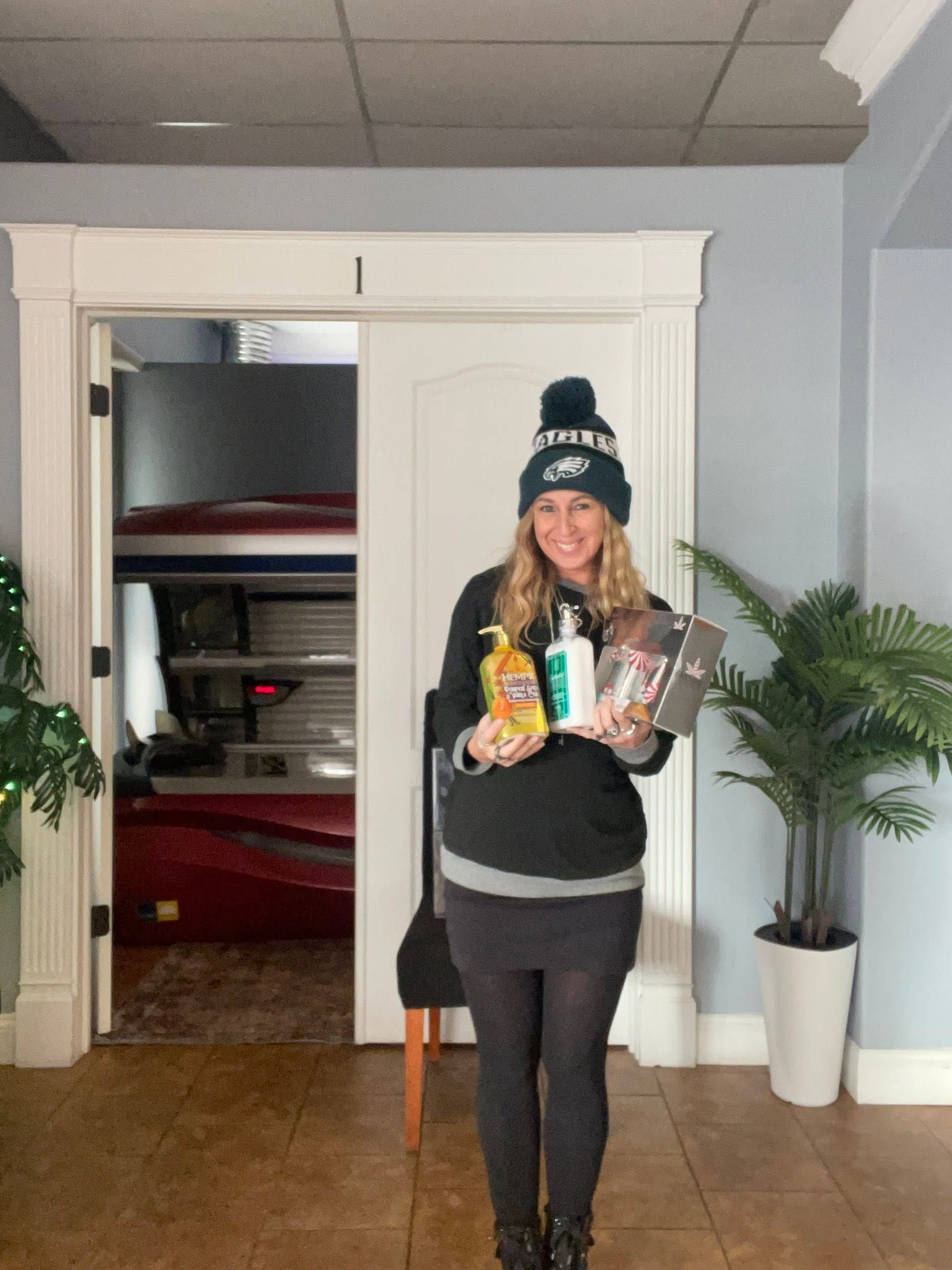 Person in a doorway holding groceries, wearing a winter hat and smiling.