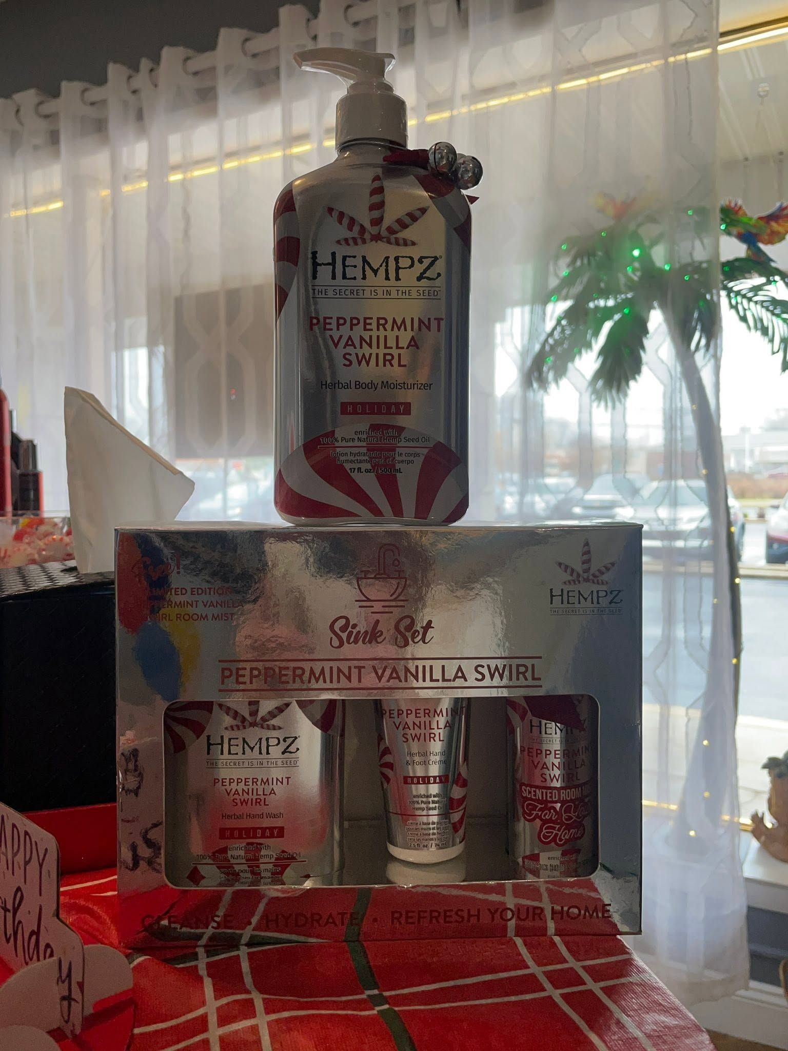 Gift basket of Hempz body care products in red packaging displayed by a window with sheer curtains.