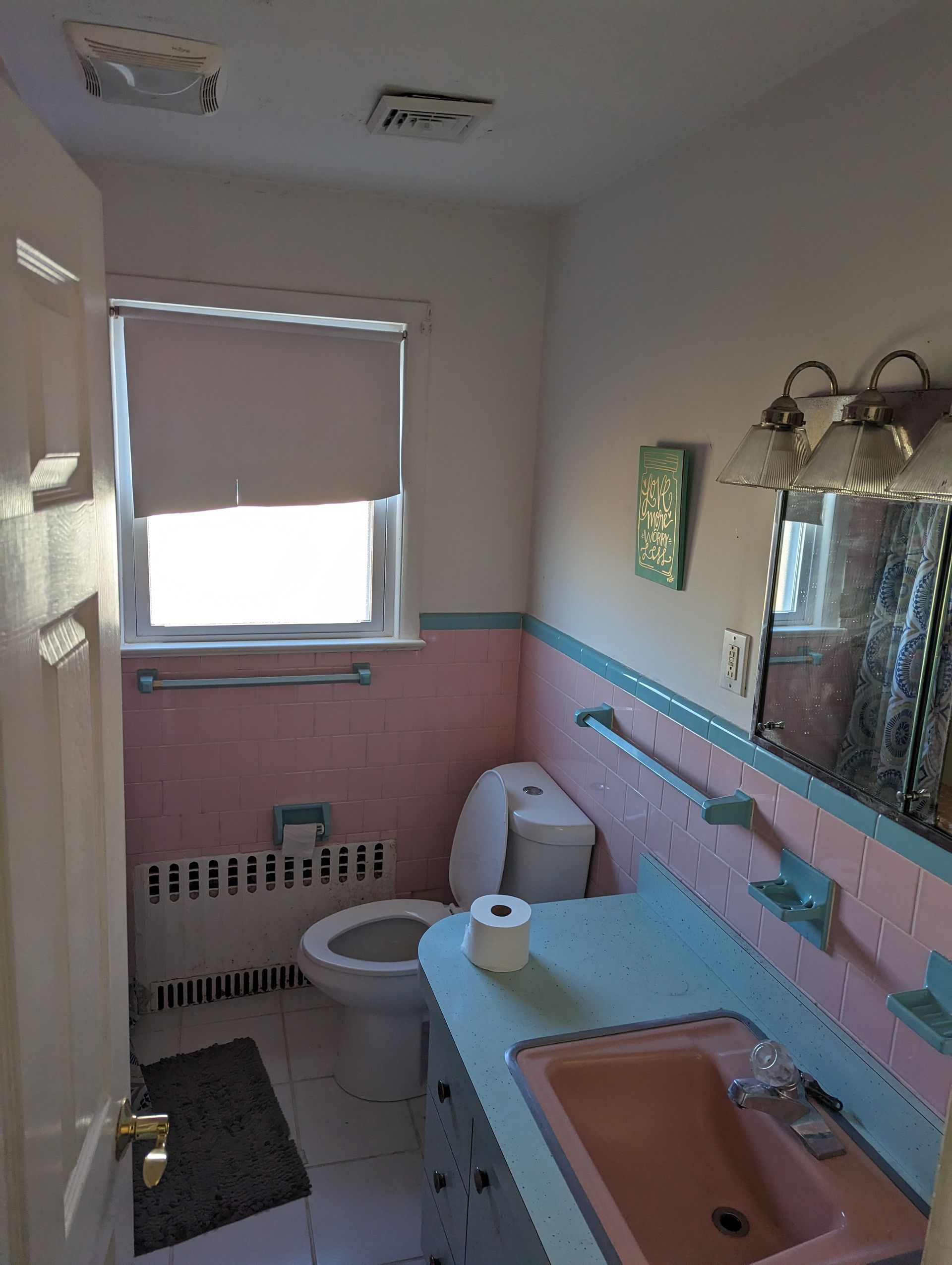 a bathroom with a toilet , sink , mirror and window .