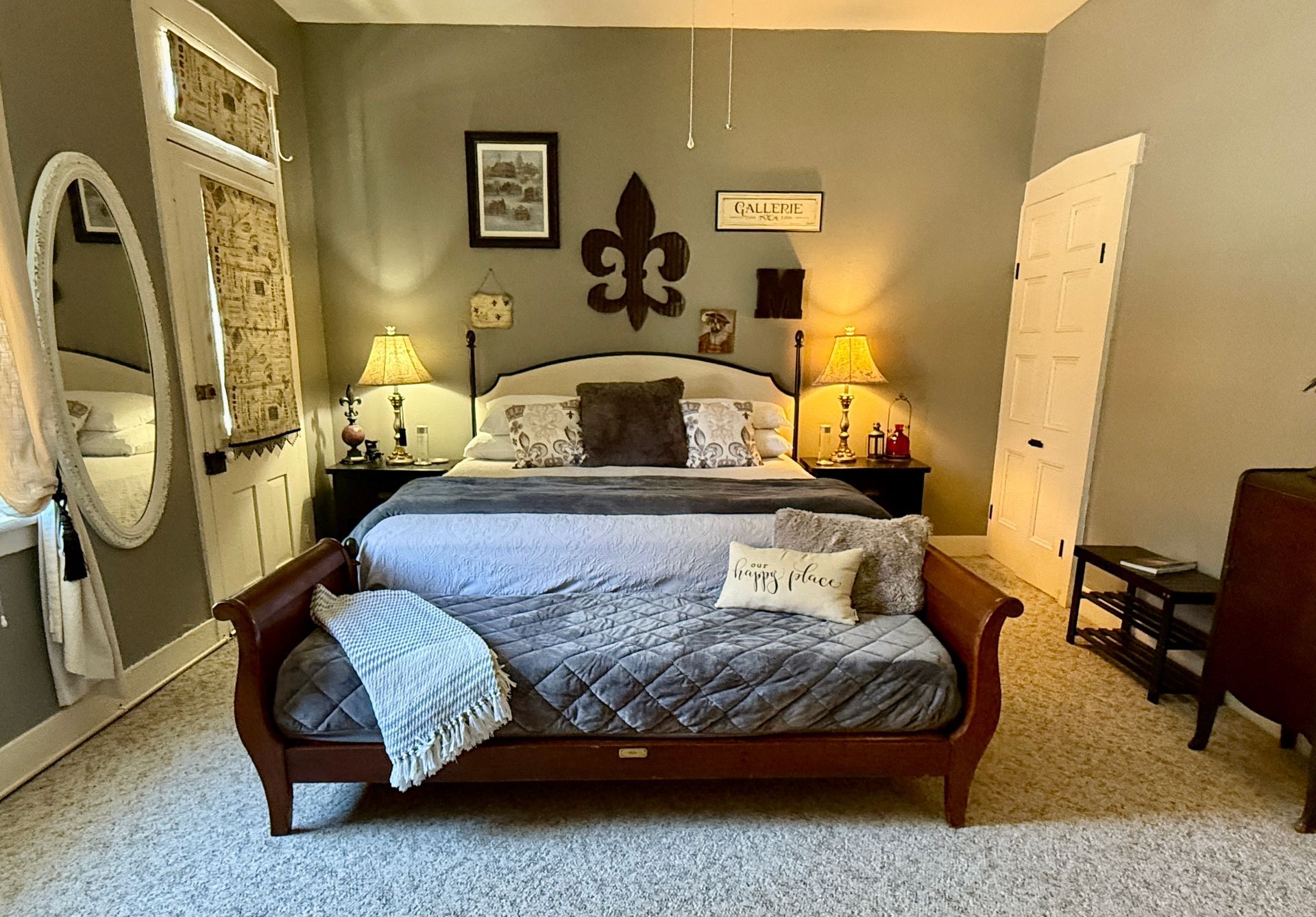 Bedroom with a dark wooden bed, gray bedding, and a fleur-de-lis wall decoration.