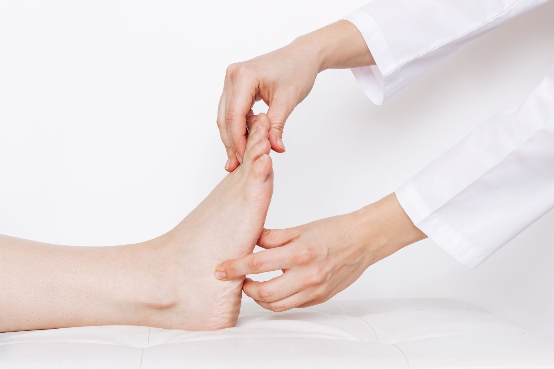 Hands examine a foot, person lying down. White coat, medical setting.