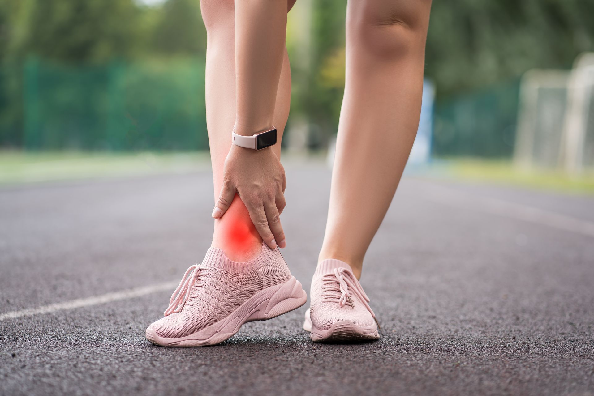 Woman on a track, holding her ankle, which is highlighted with a red circle, showing injury.