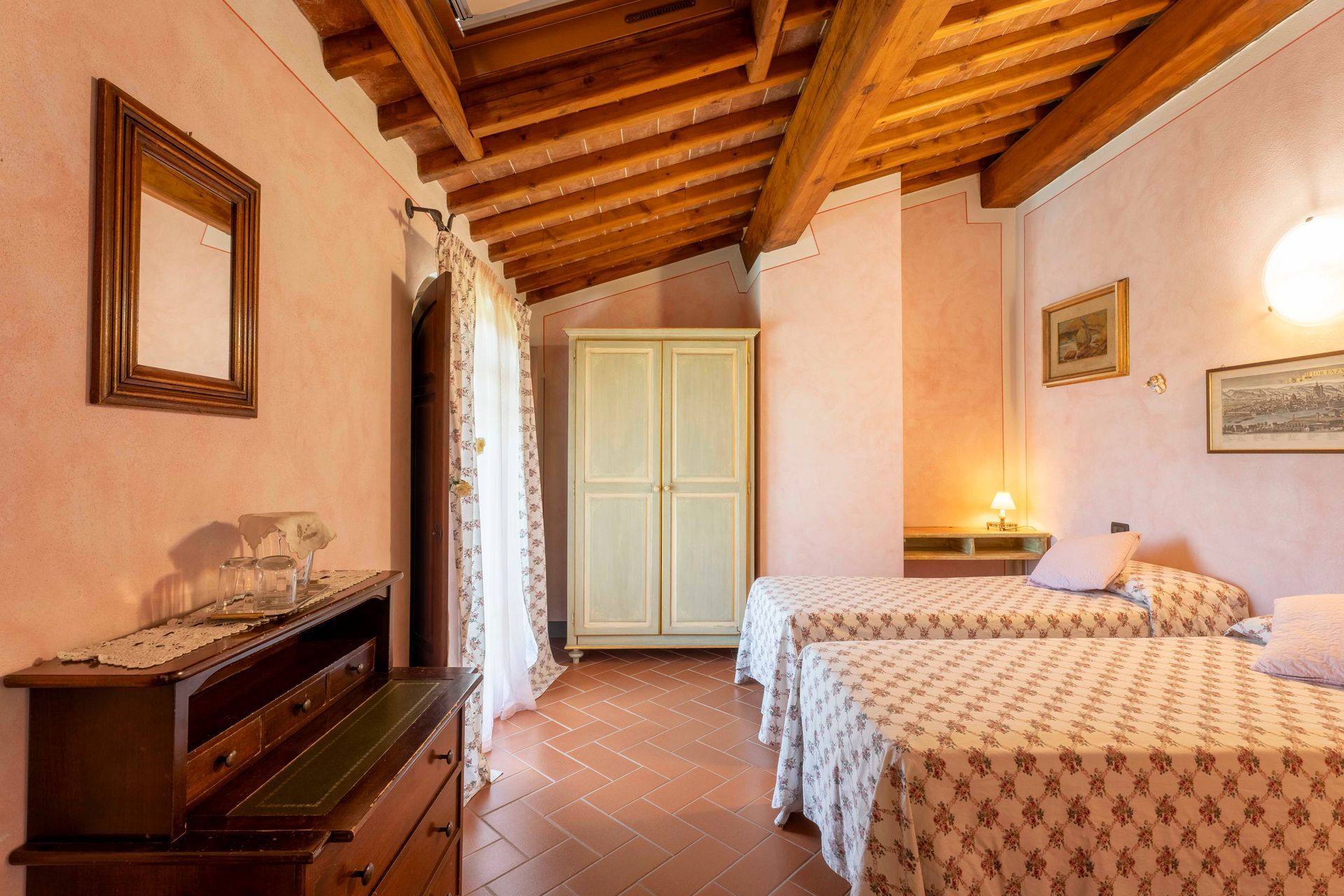Accogliente camera da letto in stile rustico con travi a vista, due letti singoli, comò e luce soffusa e calda.