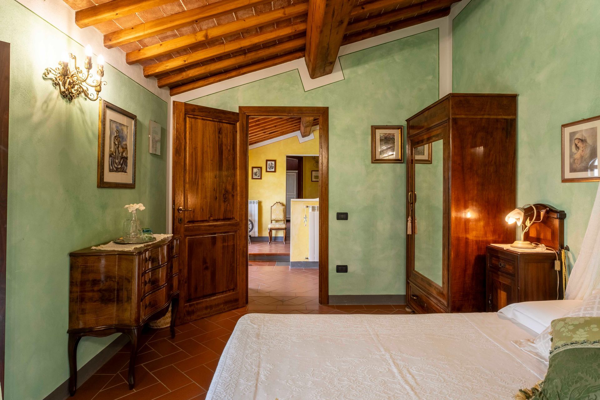 Camera da letto rustica con travi in legno, pareti verdi, porte aperte e un letto in primo piano.