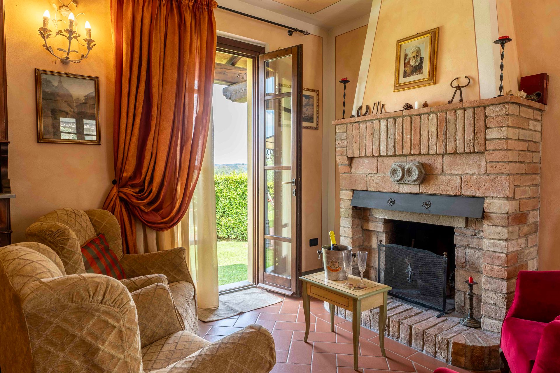 Accogliente soggiorno con camino in mattoni, tende arancioni, sedie decorate e porte aperte sul giardino.
