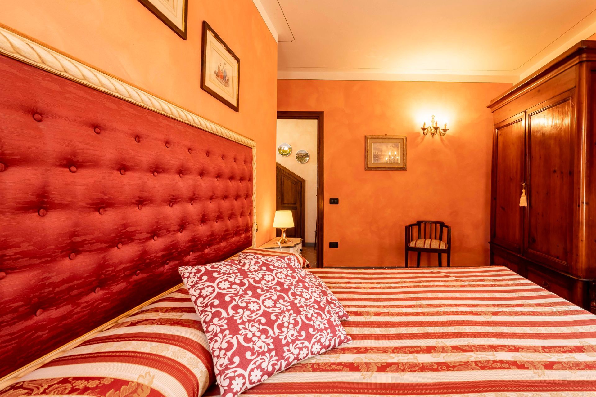 Letto rosso trapuntato in una camera da letto color arancio caldo con biancheria da letto a righe e armadio in legno.
