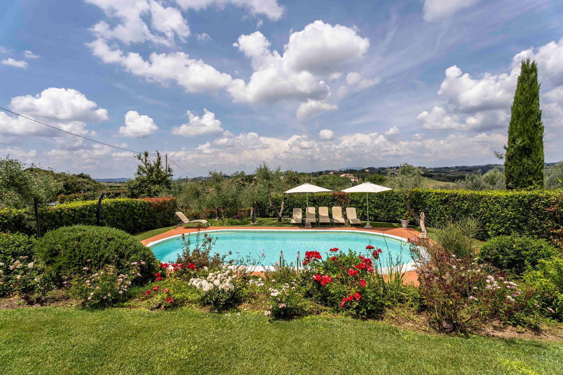 Piscina paesaggistica del resort con ombrelloni, fiori e verdi colline sotto un cielo nuvoloso.