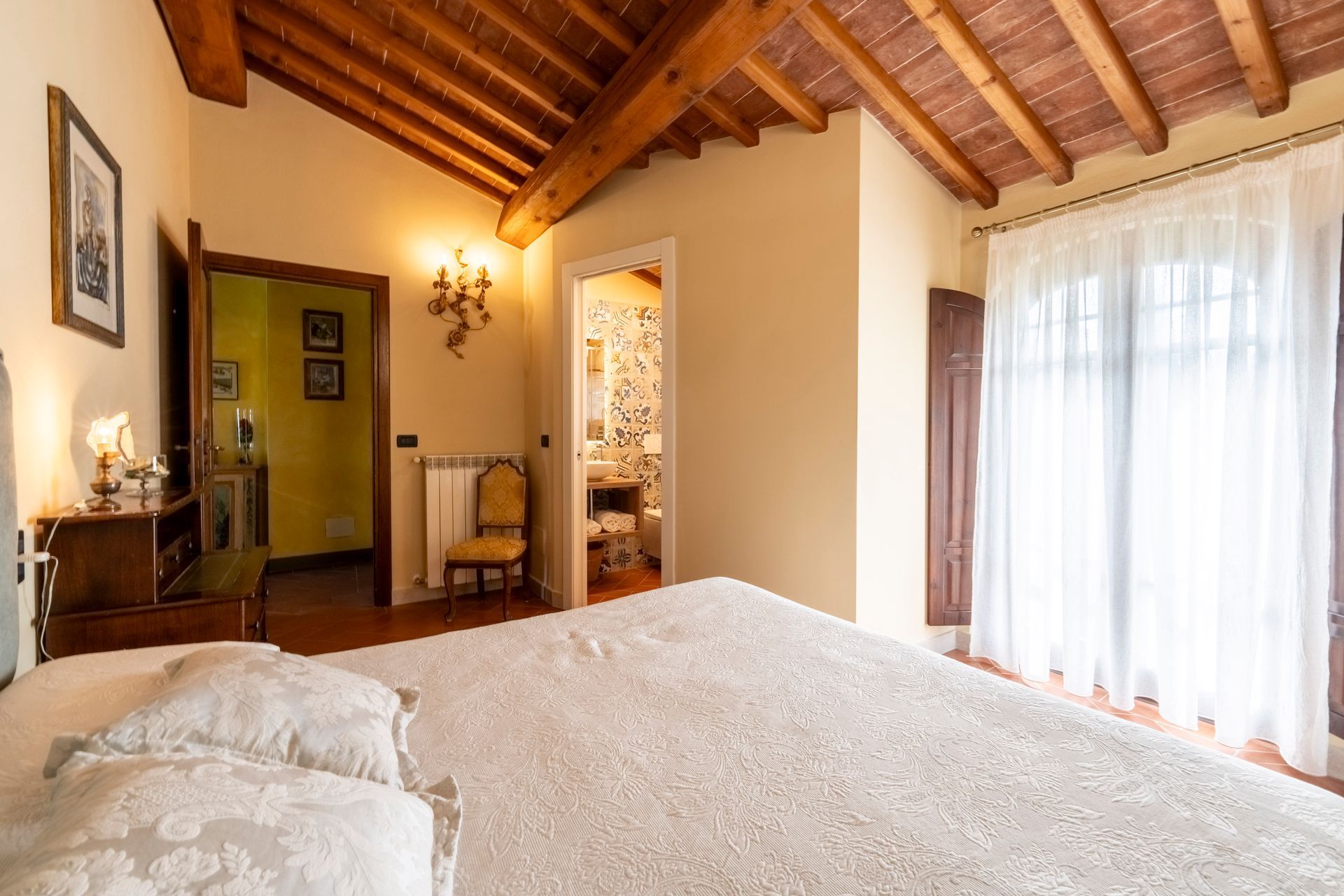 Accogliente camera da letto con copriletto floreale, mobili in legno, travi a vista e calda luce di lampada.