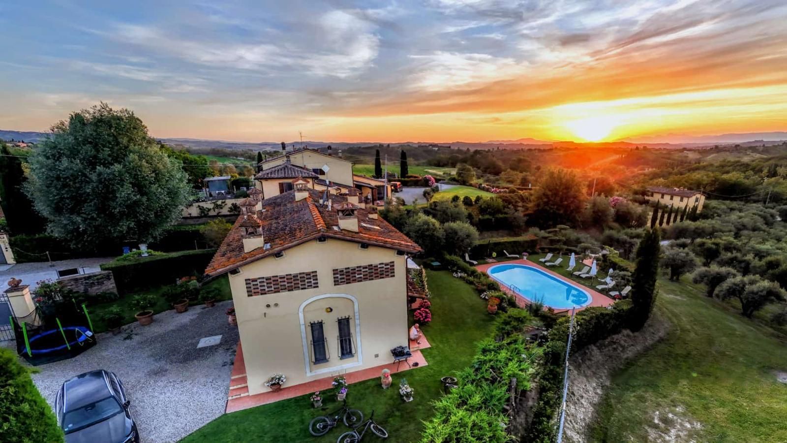 Piscina con lettini, ombrelloni bianchi e una rigogliosa vista sul giardino sotto un cielo nuvoloso.