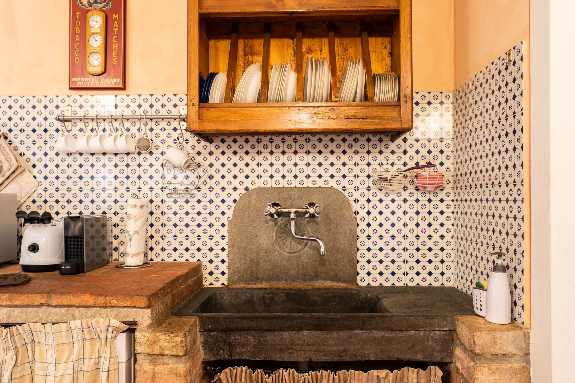 Lavello da cucina rustico con paraschizzi in piastrelle a mosaico, mensole in legno ed elettrodomestici da banco.
