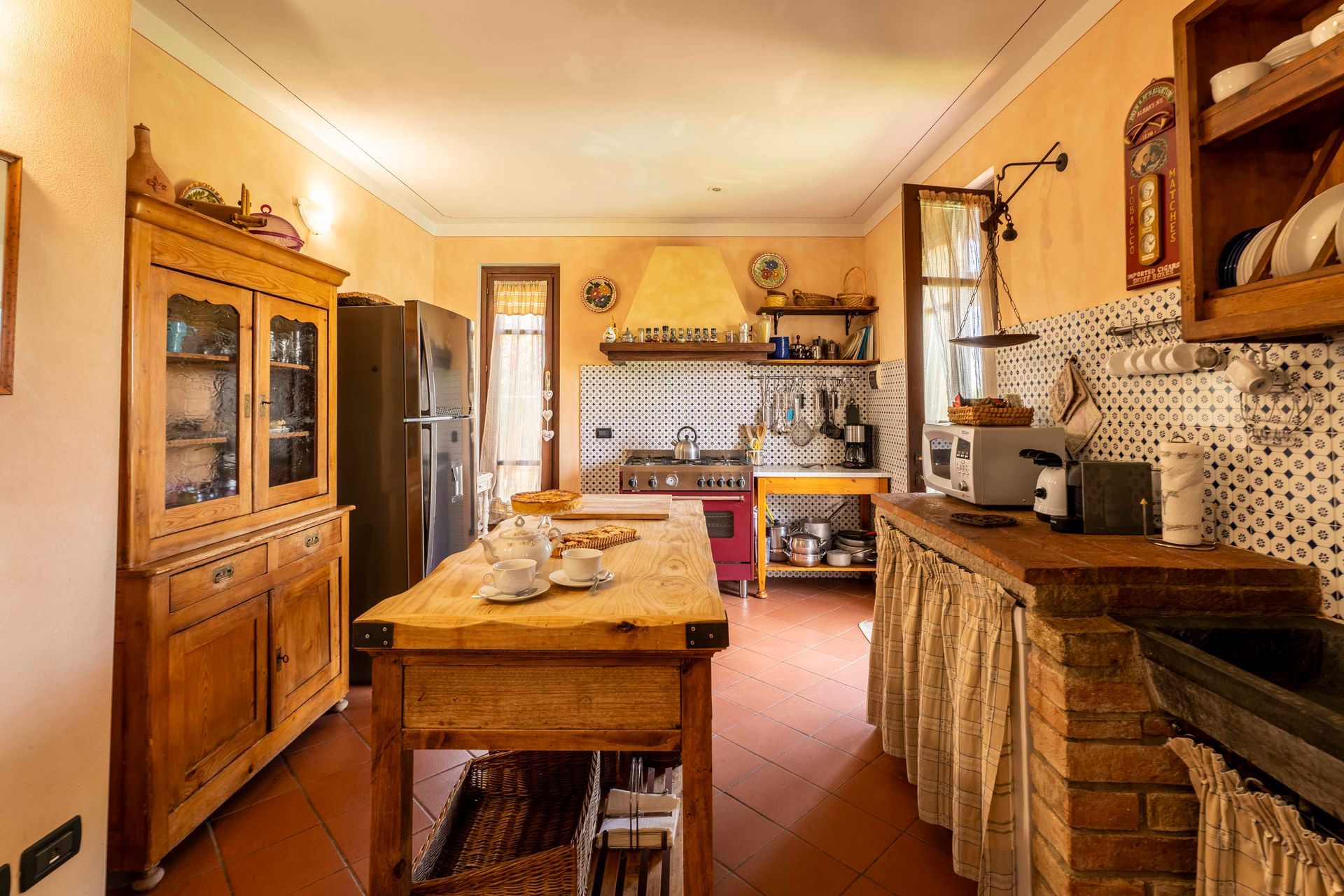 Cucina rustica con mobili in legno, isola centrale, piastrelle decorate e luce naturale calda.