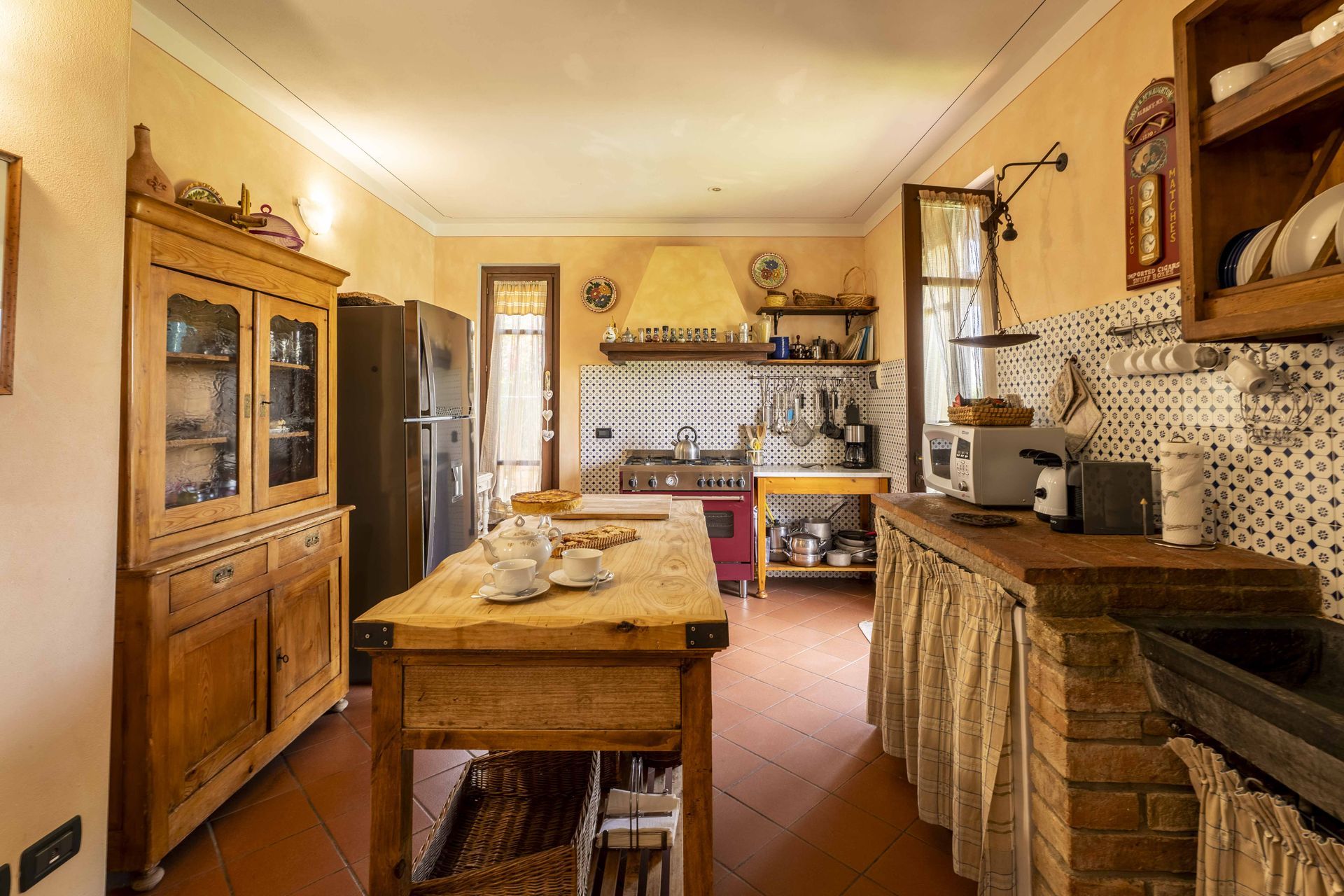 Cucina rustica con mobili in legno, tavolo centrale, paraschizzi piastrellato e pareti color giallo caldo.