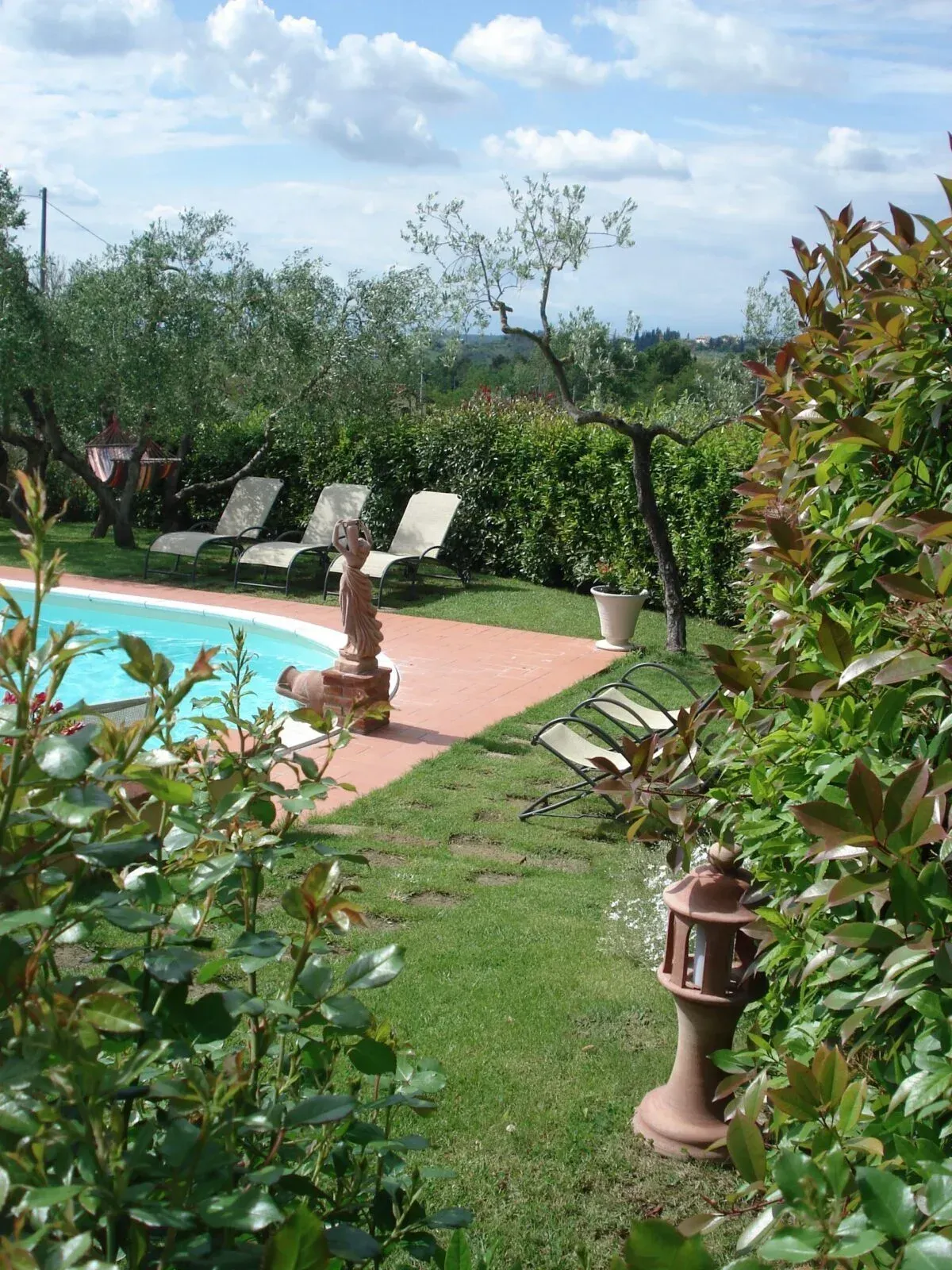 Piscina in giardino con lettini, prato verde e piante in vaso sotto un cielo nuvoloso.