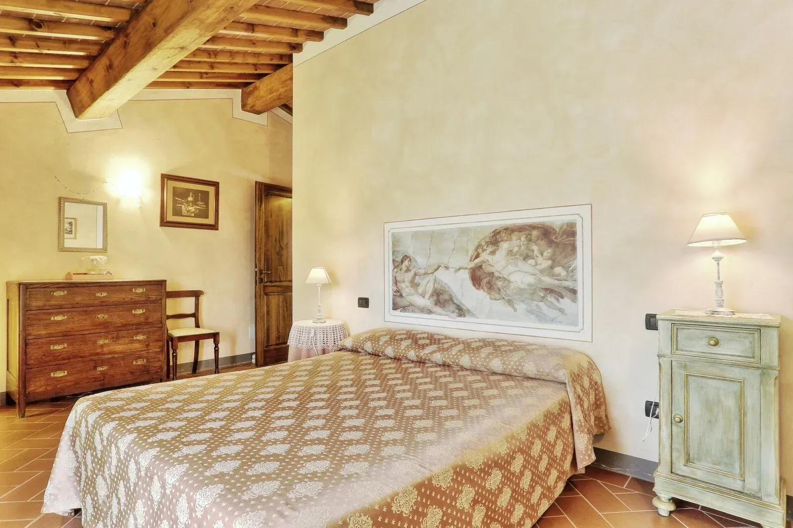 Accogliente camera da letto con soffitto in legno, copriletto a fantasia, comò e due lampade da comodino.