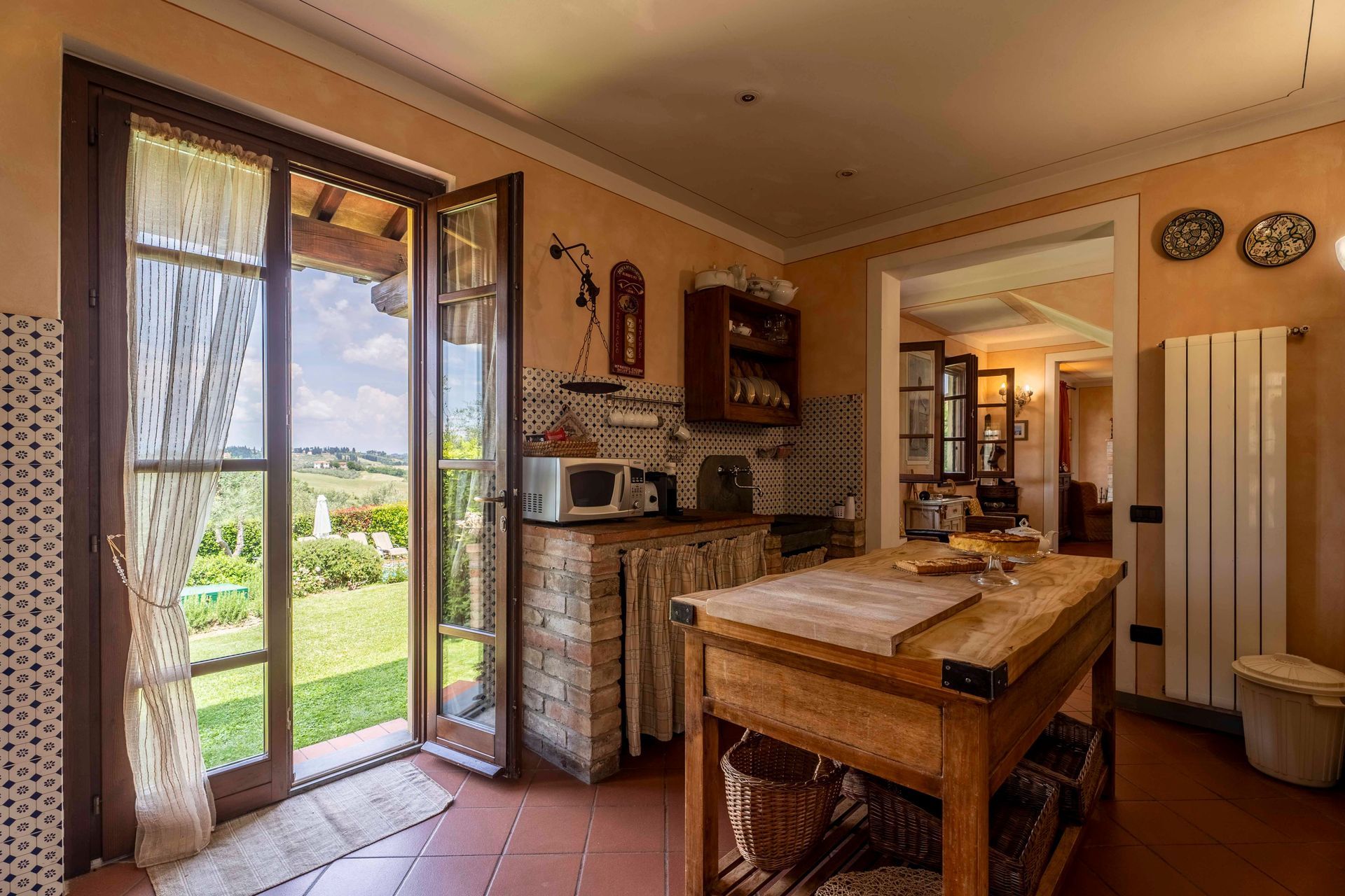 Cucina rustica con tavolo in legno, porta aperta sul giardino e calda luce del sole che filtra all'interno