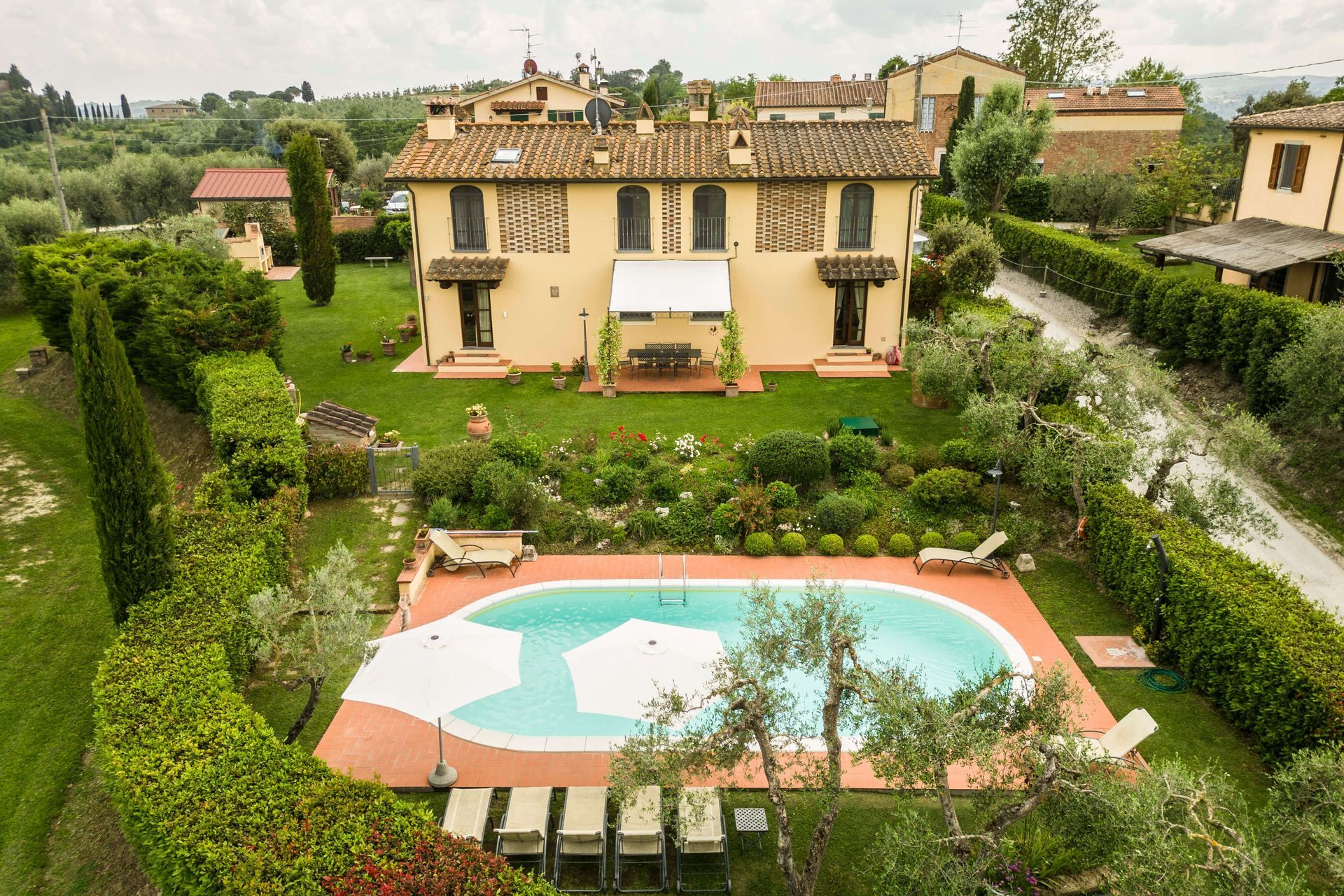 Villa con piscina turchese, circondata da siepi rigogliose e un cortile con giardino.