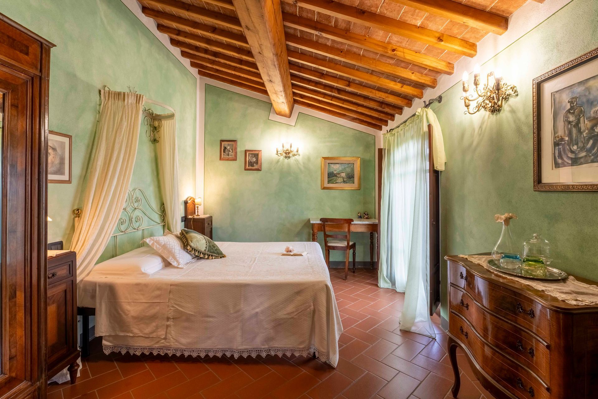 Camera da letto rustica con pareti verdi, travi in legno, letto, comò e tende luminose.