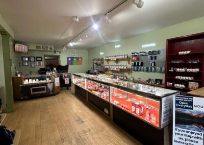 A well-lit cannabis dispensary with a wooden floor, glass display cases filled with products, and shelves on the wall.