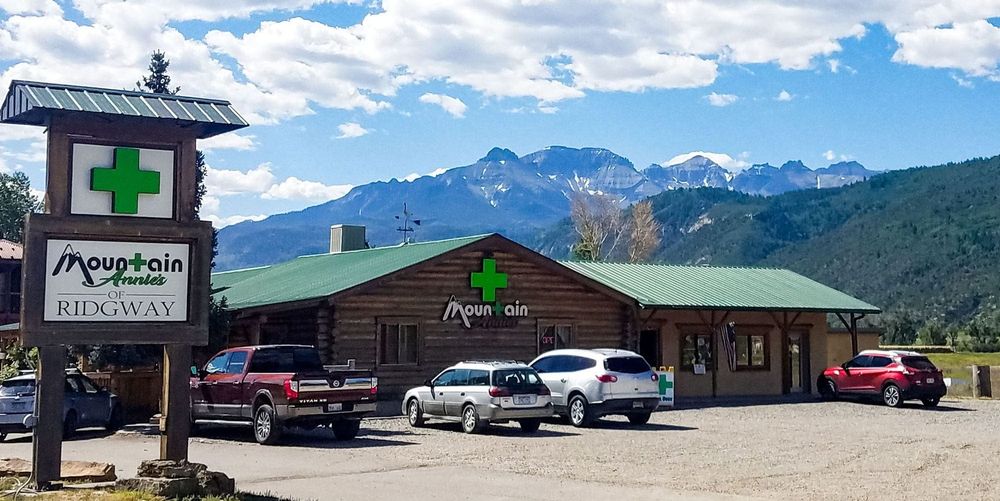 Mountain Medicine cannabis dispensary in a log cabin style building under a mountain range with several cars in the lot.