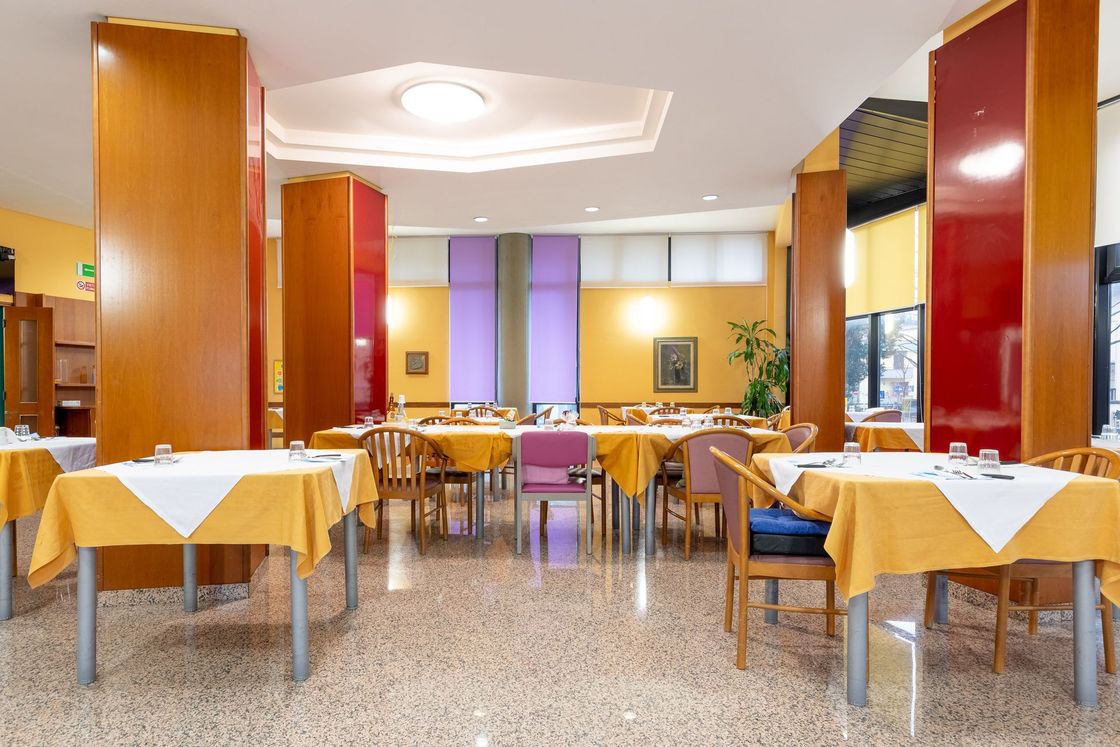 Sala da pranzo di un ristorante moderno, con tovaglie gialle, colonne in legno e pannelli colorati alle pareti