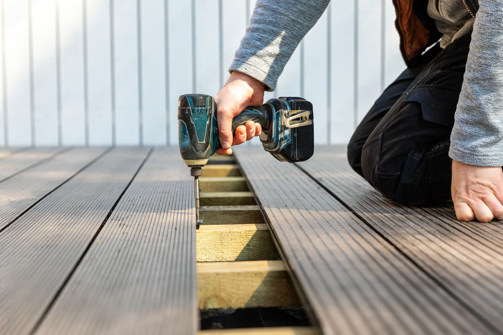 a man is installing a wooden deck with a drill .