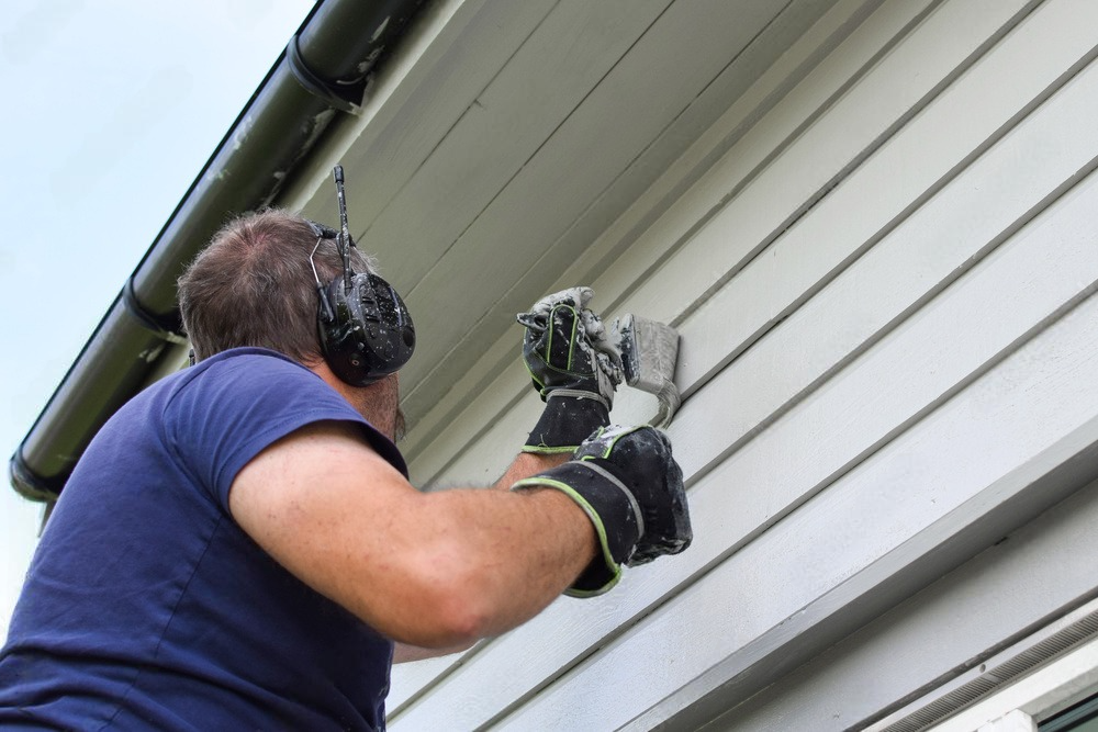 a man wearing headphones and gloves is working on the side of a house .