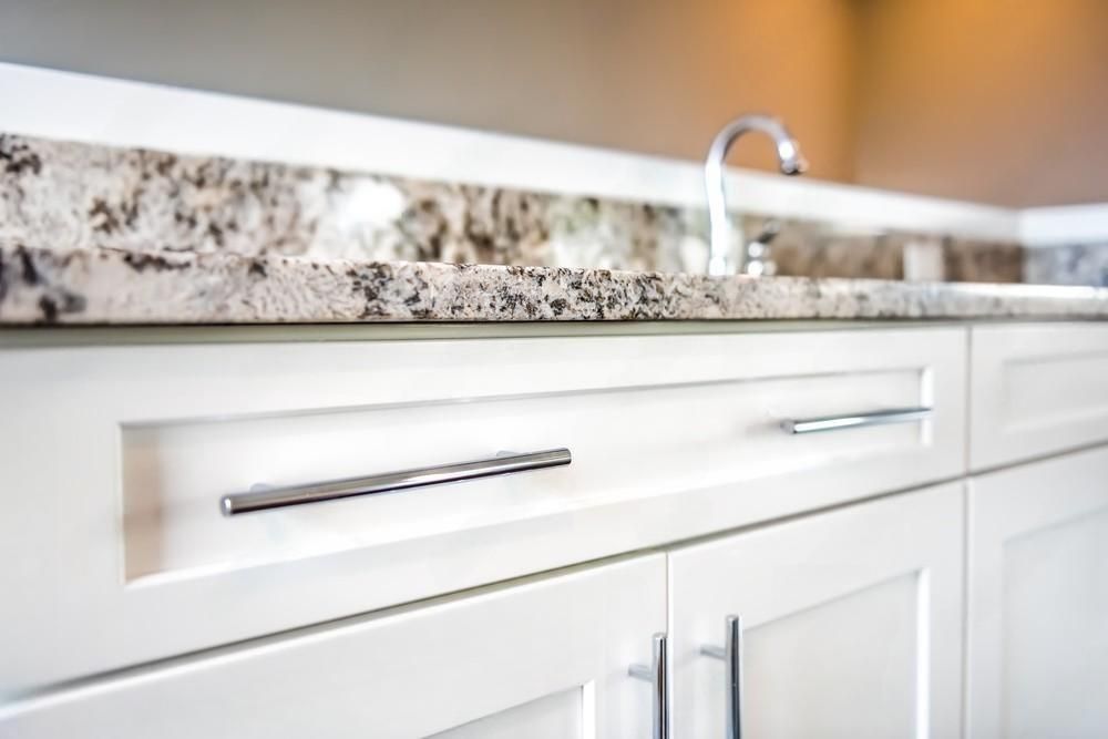 a kitchen sink with a granite counter top and white cabinets .