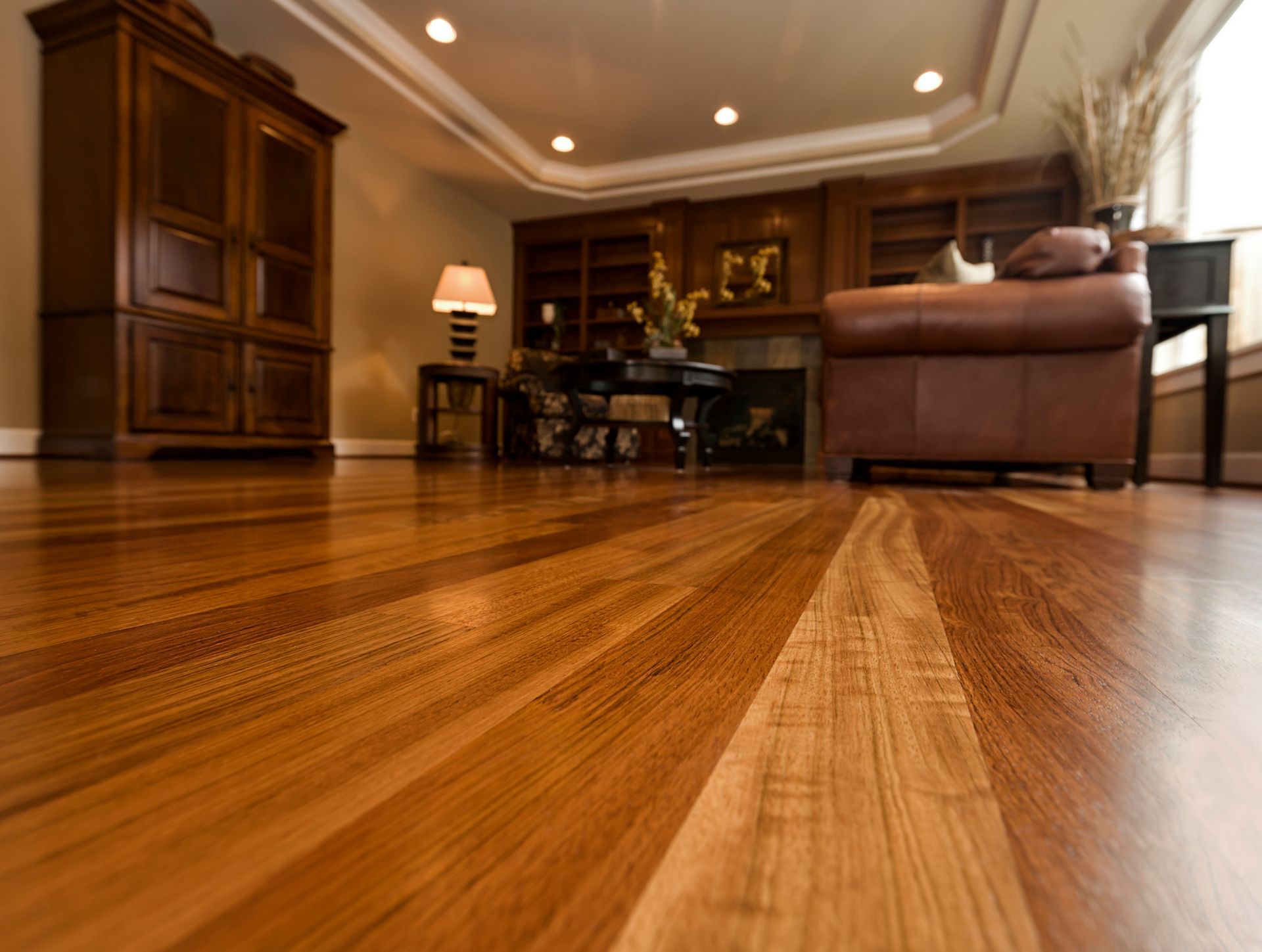 Wooden floor in a room with a brown leather couch, cabinet, and recessed lighting.