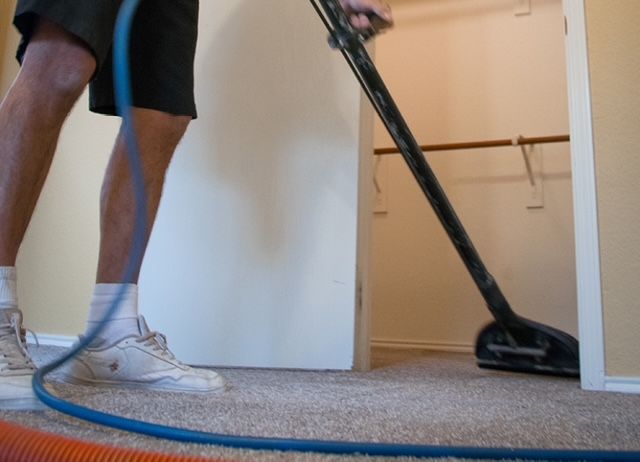 Person vacuuming carpet inside a closet; blue hose and black vacuum head.
