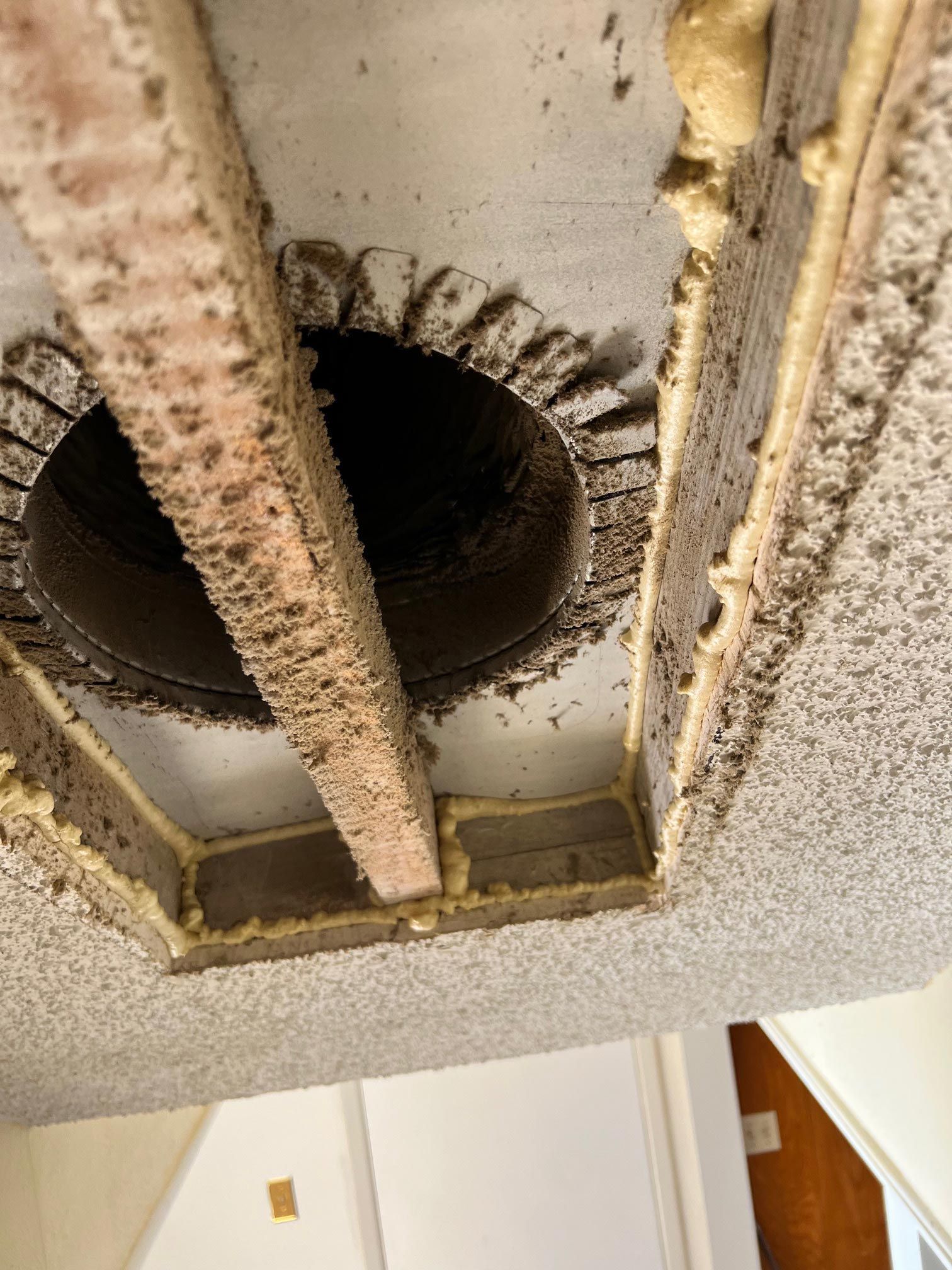 Ceiling air vent covered in dust and debris, framed by wooden supports and insulation. Ceiling air vent covered in dust and debris, framed by wooden supports and insulation.