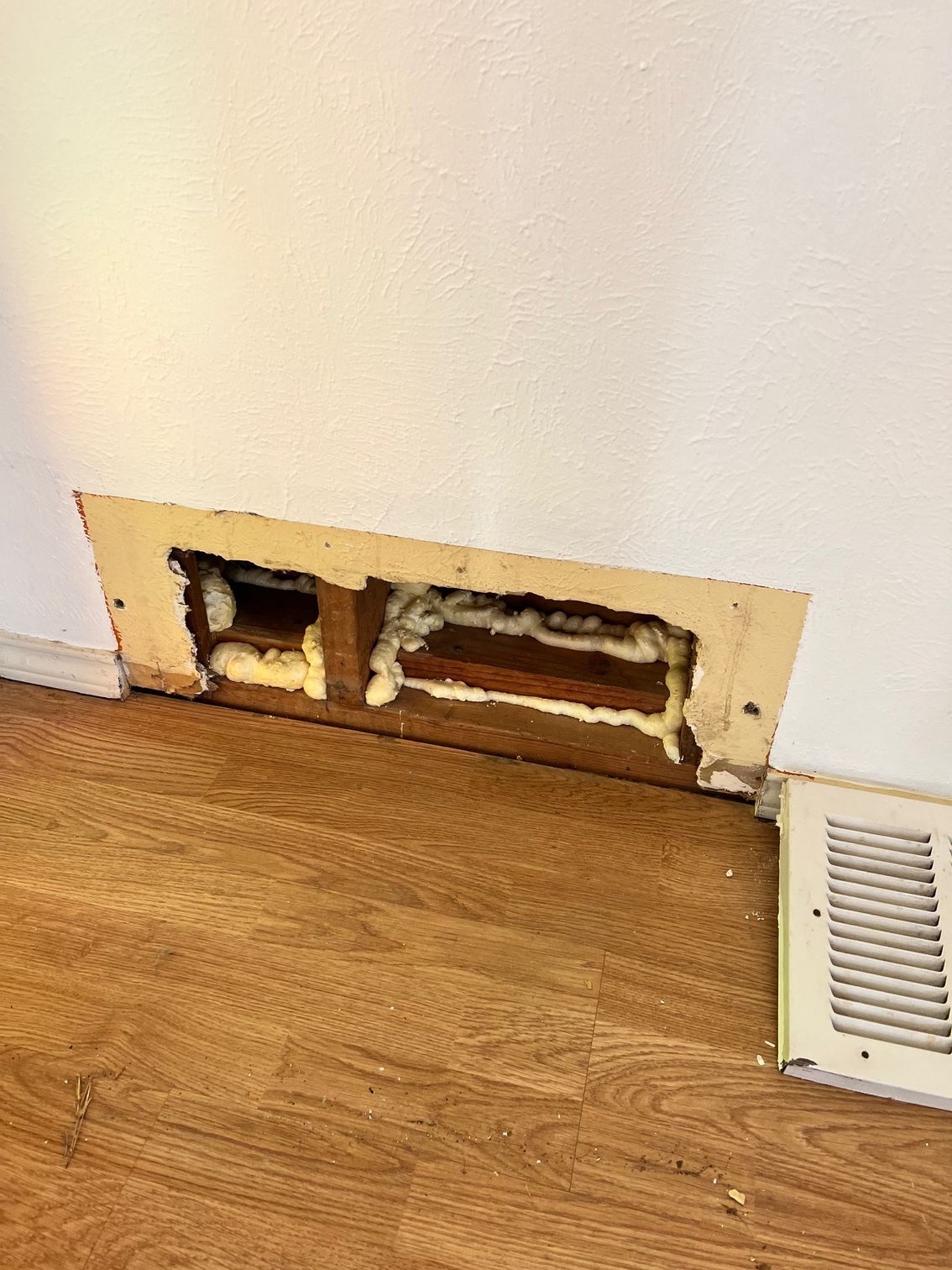 Wall vent sealed with spray foam, next to a floor vent. The floor is wood-look laminate. Wall vent sealed with spray foam, next to a floor vent. The floor is wood-look laminate.