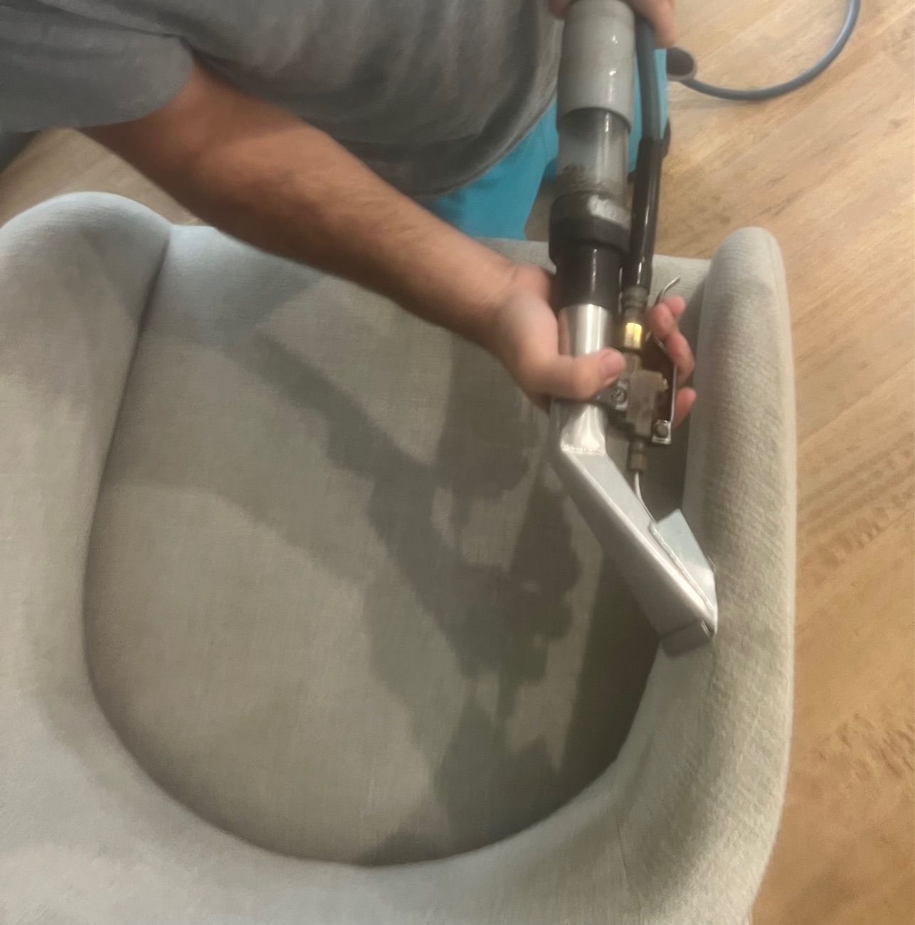 Person cleaning a light gray armchair with a steam cleaner.