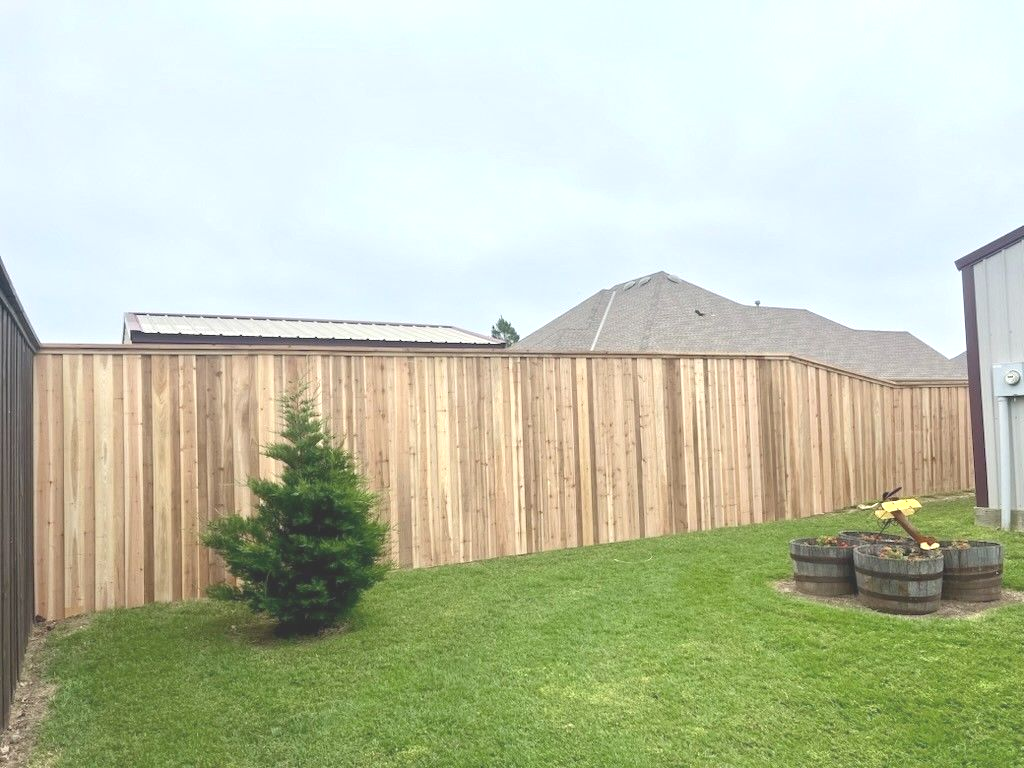Wooden privacy fence in a grassy backyard, small tree, and a barrel fire pit.