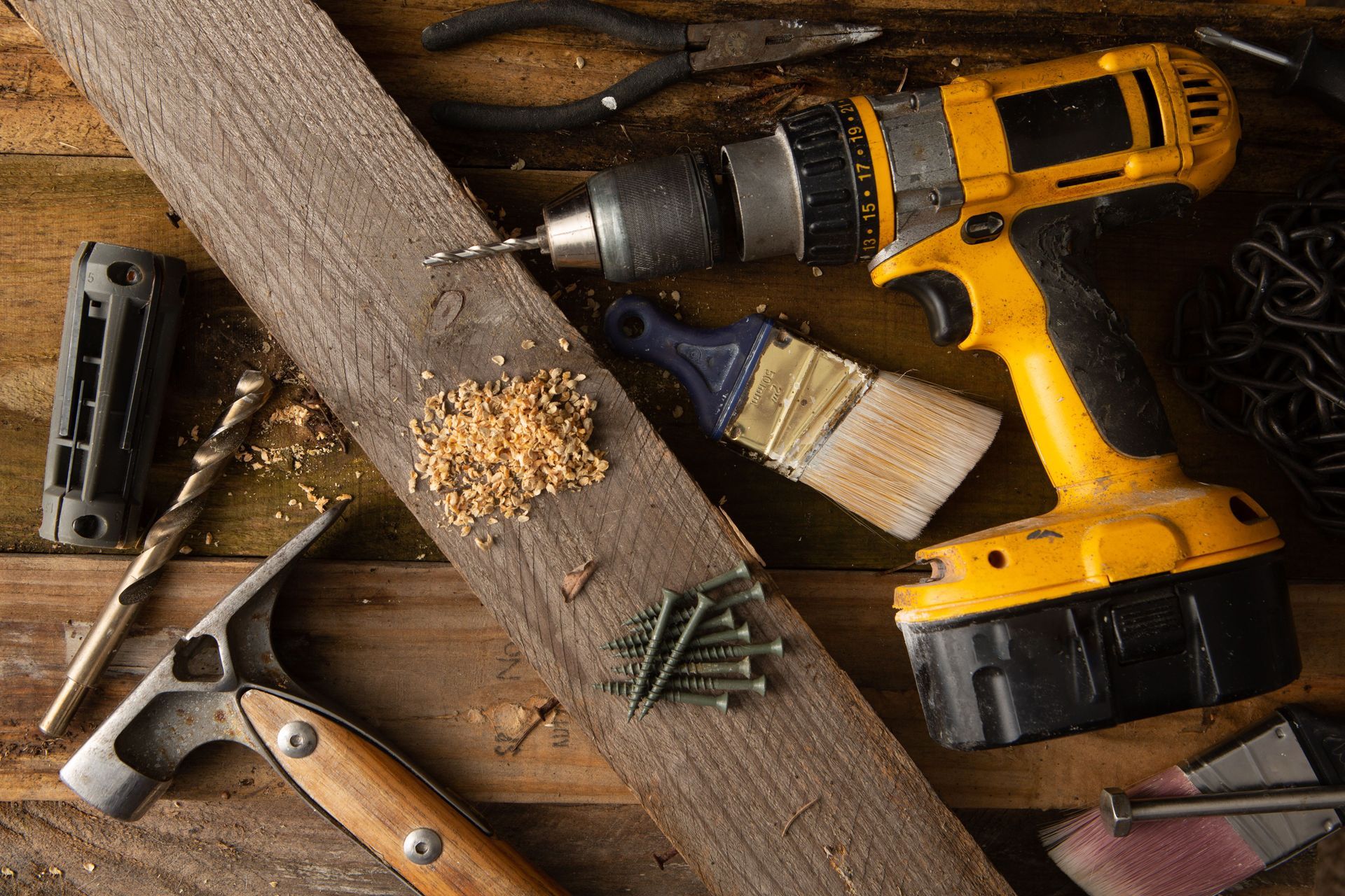 Hand tools and a yellow drill on a wooden workbench with sawdust and screws