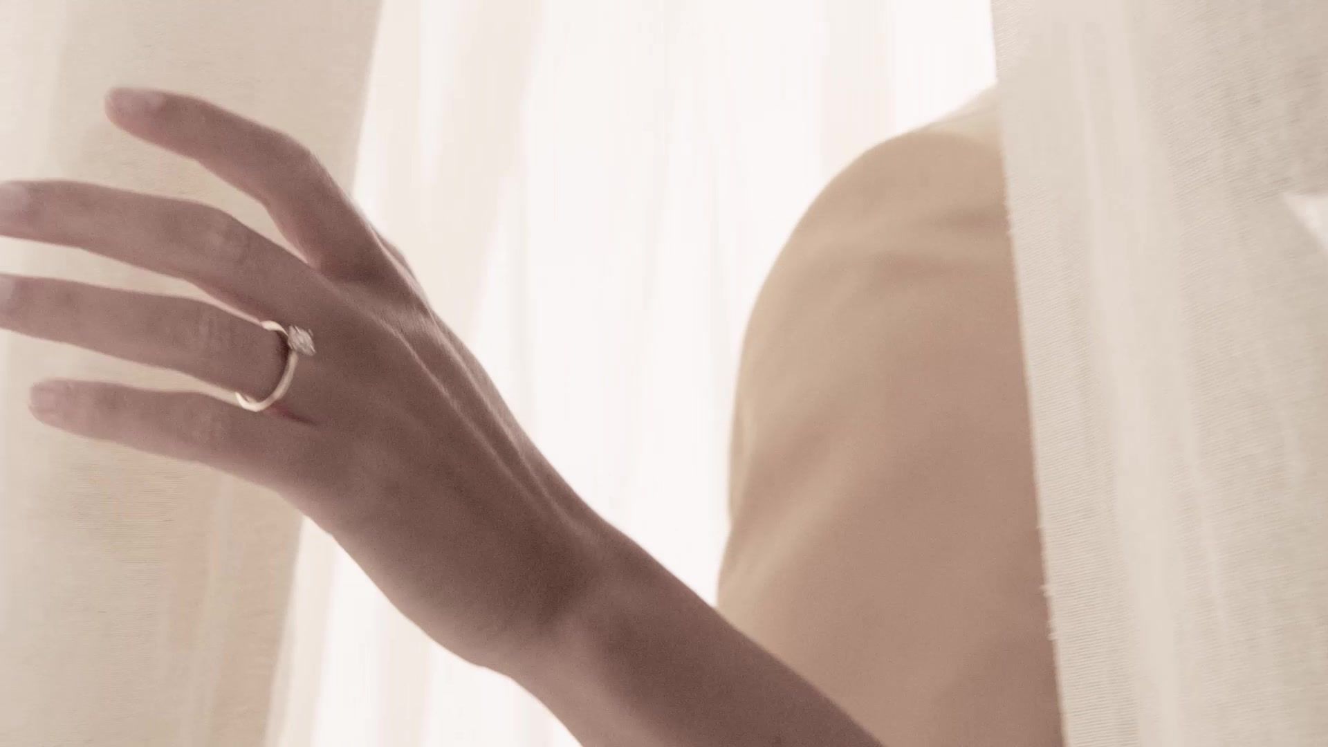 Hand met verlovingsring langs een licht gordijn