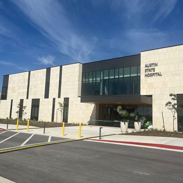 Austin State Hospital building exterior with glass entrance, cream stone facade, and yellow bollards under a blue sky