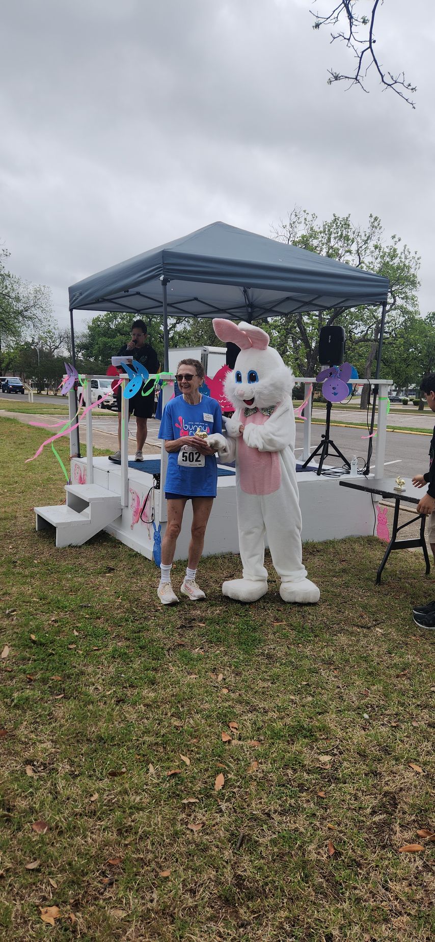 Friends of ASH race participant posing with Easter Bunny mascot on stage at an Austin outdoor fundraising event
