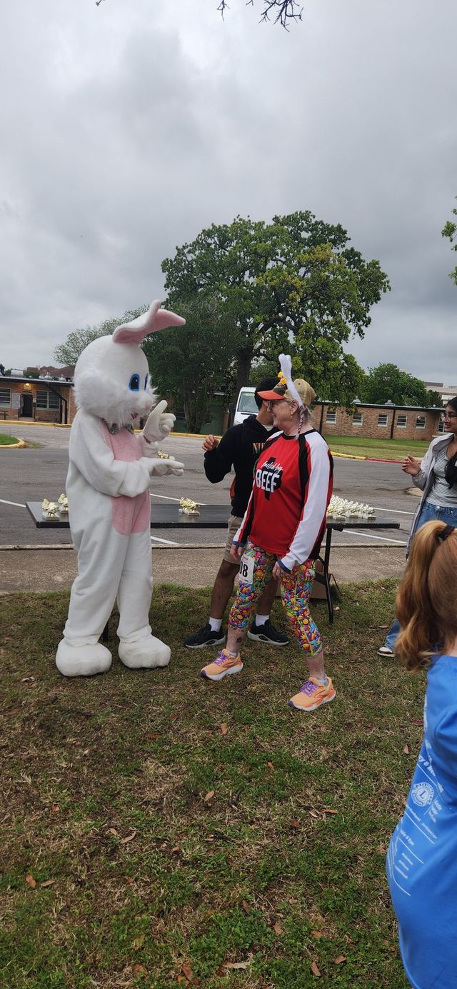 Person in bunny costume greets a child outdoors at a park with cars and trees in the background