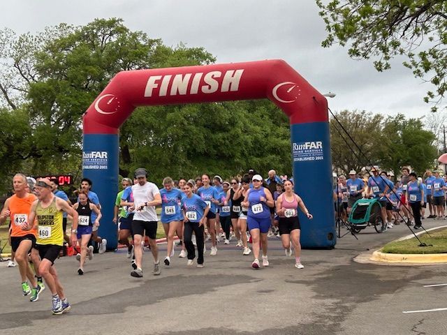 Runners crossing a red FINISH arch at a road race, with spectators and trees in the background