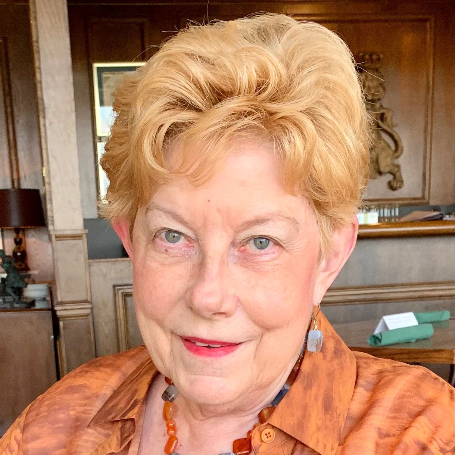 A woman with blonde hair is wearing a brown shirt and a necklace.