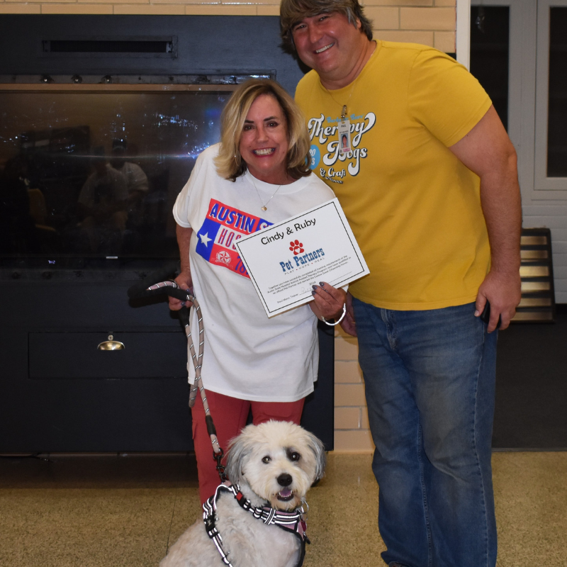 Woman holding certificate poses with man and service dog indoors