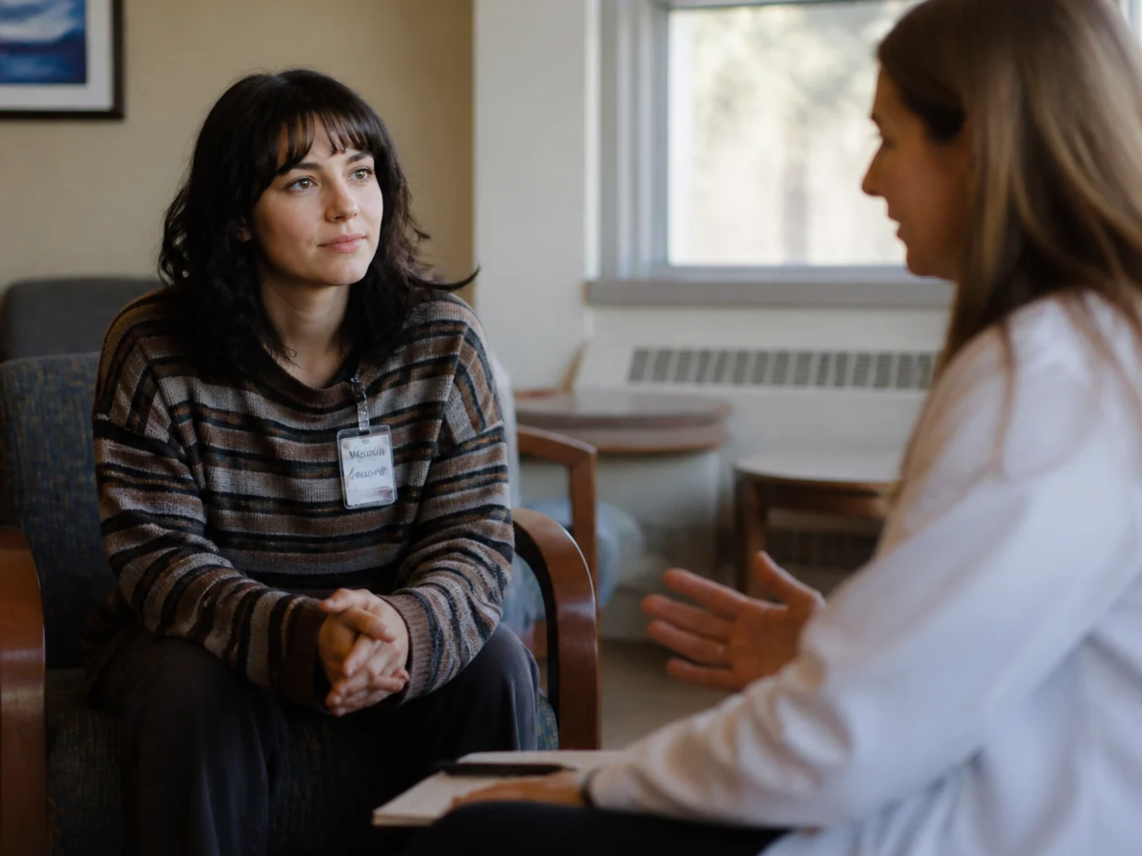 Two women in conversation during a counseling session, seated across from each other in a bright room.