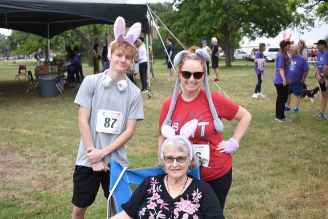 Three people posing outdoors at a race event, one with bunny ears and one in a wheelchair.