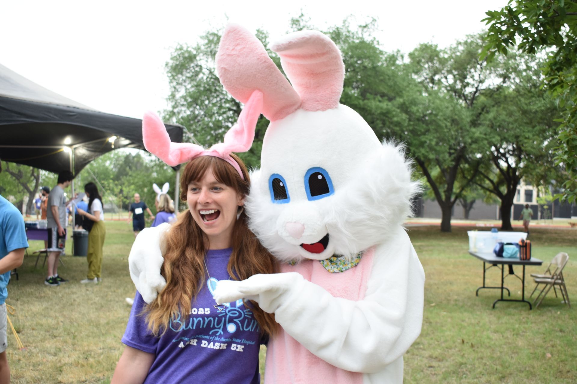 Friends of ASH race participant posing with Easter Bunny mascot on stage at an Austin outdoor fundraising event
