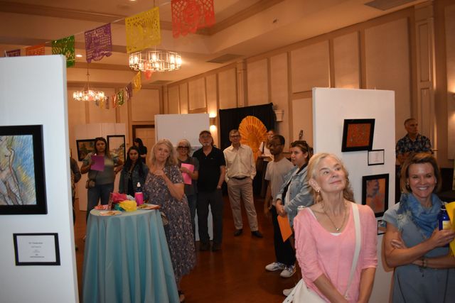 Guests mingle at an indoor art gallery reception with colorful decorations and displayed paintings.