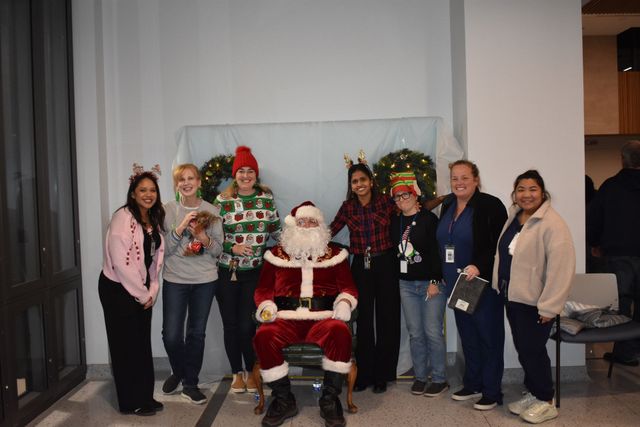 Group posing with Santa and festive holiday figures in front of a white backdrop